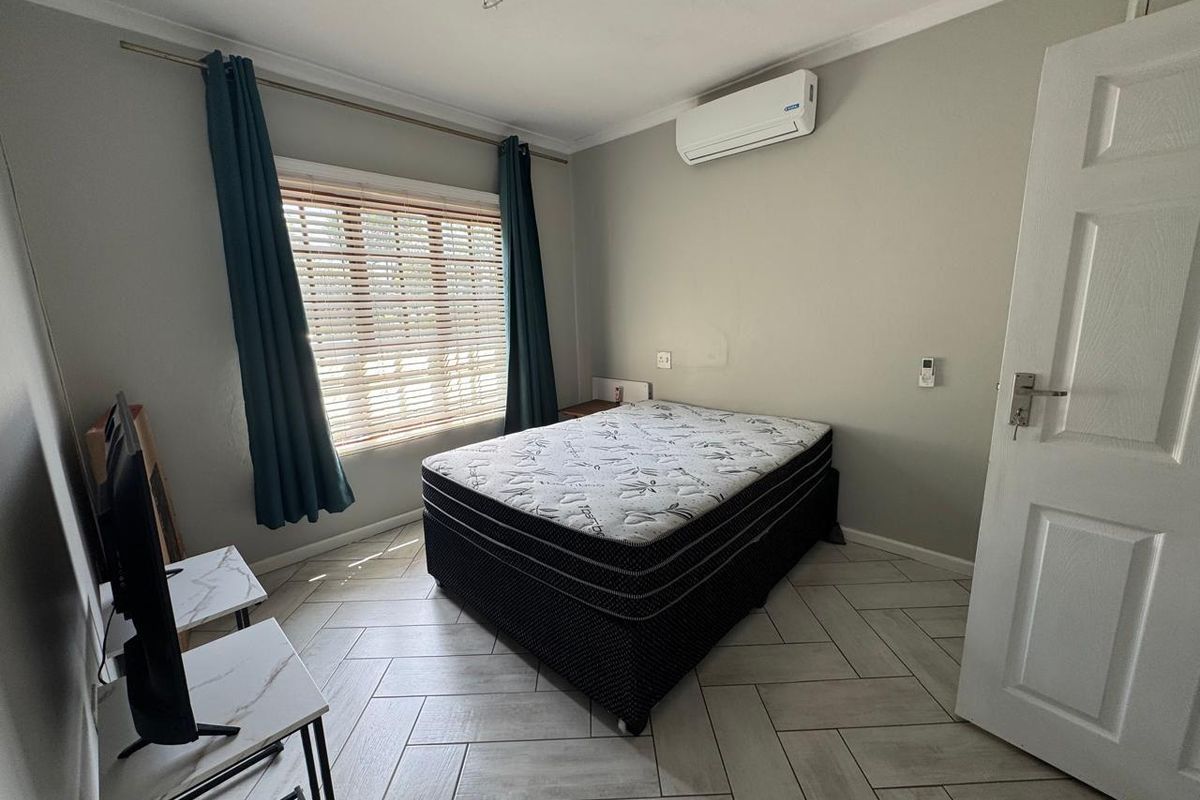 A well-lit bedroom featuring modern tiled flooring, a wall-mounted air conditioning unit, and neutral wall finishes.