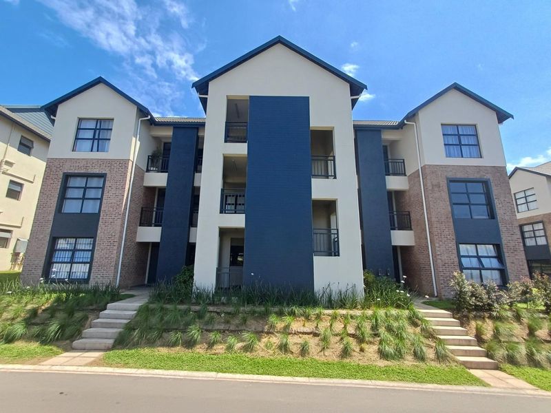 A modern multi-story apartment building featuring a combination of brick and painted facade, private balconies, and landscaped front access stairs.