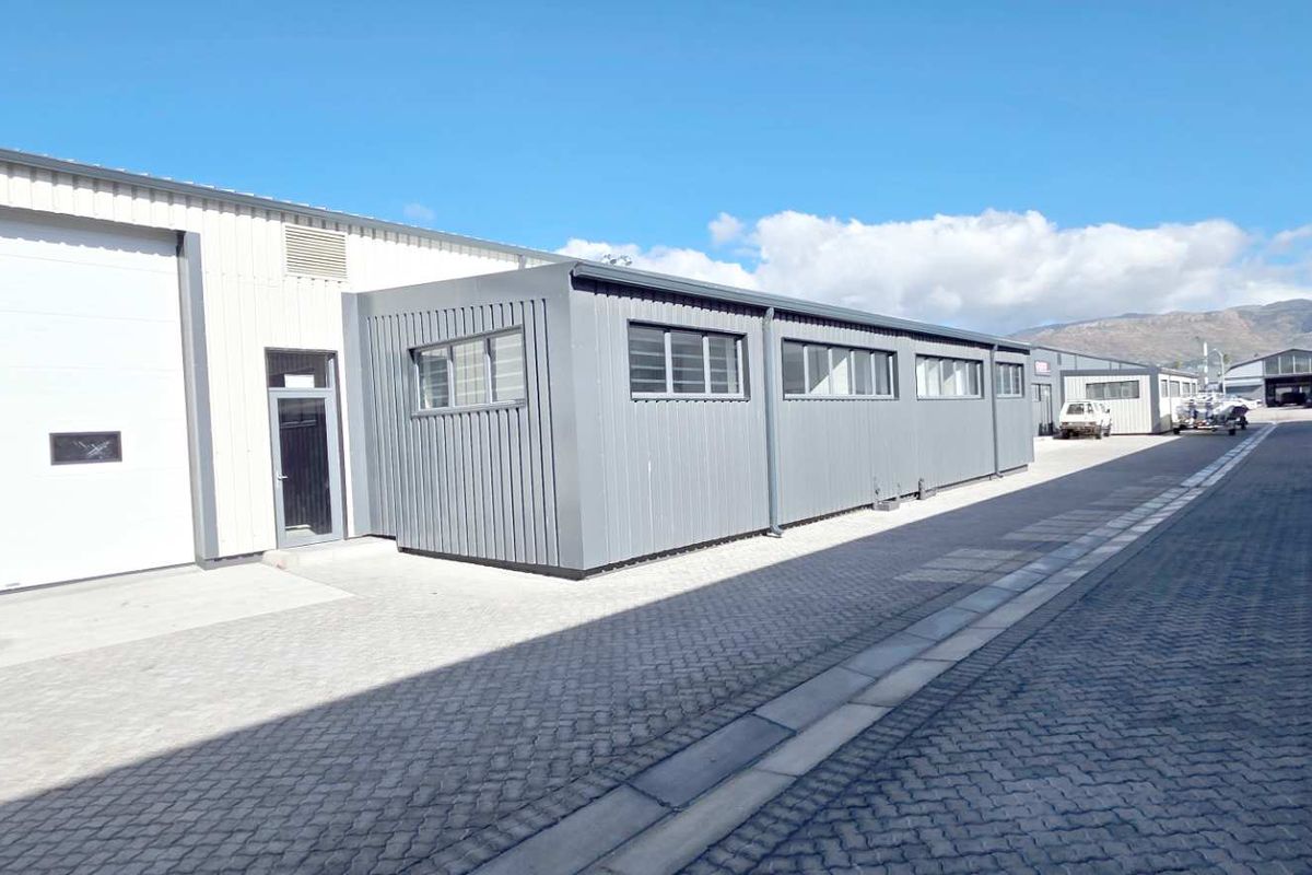 Exterior view of an industrial warehouse complex featuring metal cladding, roller shutter doors, and paved driveway access.
