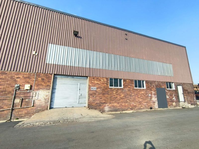 Industrial warehouse exterior featuring a brick facade, corrugated metal cladding, and a roller shutter door with an asphalt driveway approach.