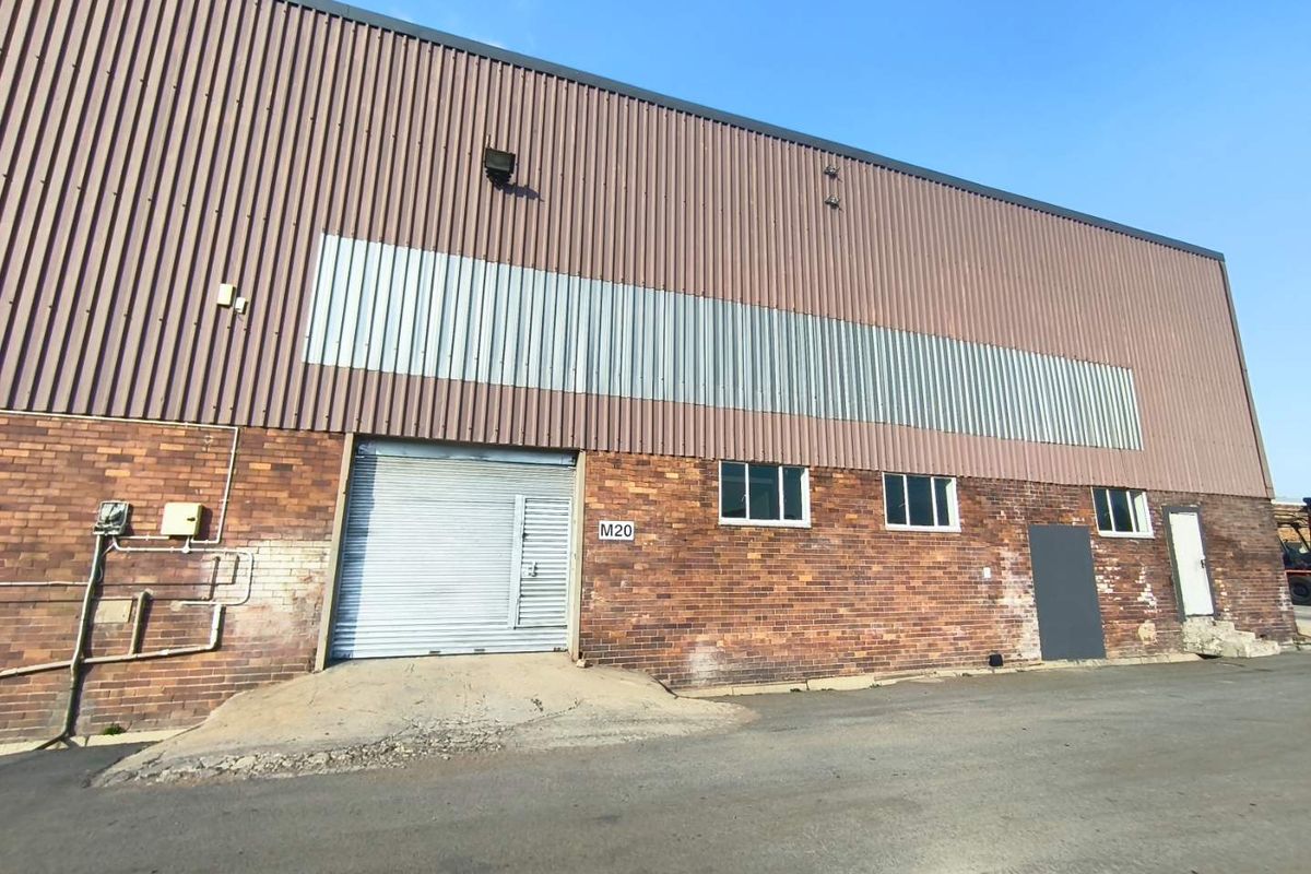 Industrial warehouse exterior featuring a brick facade, corrugated metal cladding, and a roller shutter door with an asphalt driveway approach.