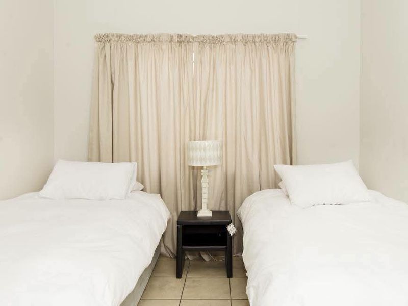 A simple bedroom featuring neutral wall tones, tiled flooring, and a window dressed with floor-to-ceiling curtains.