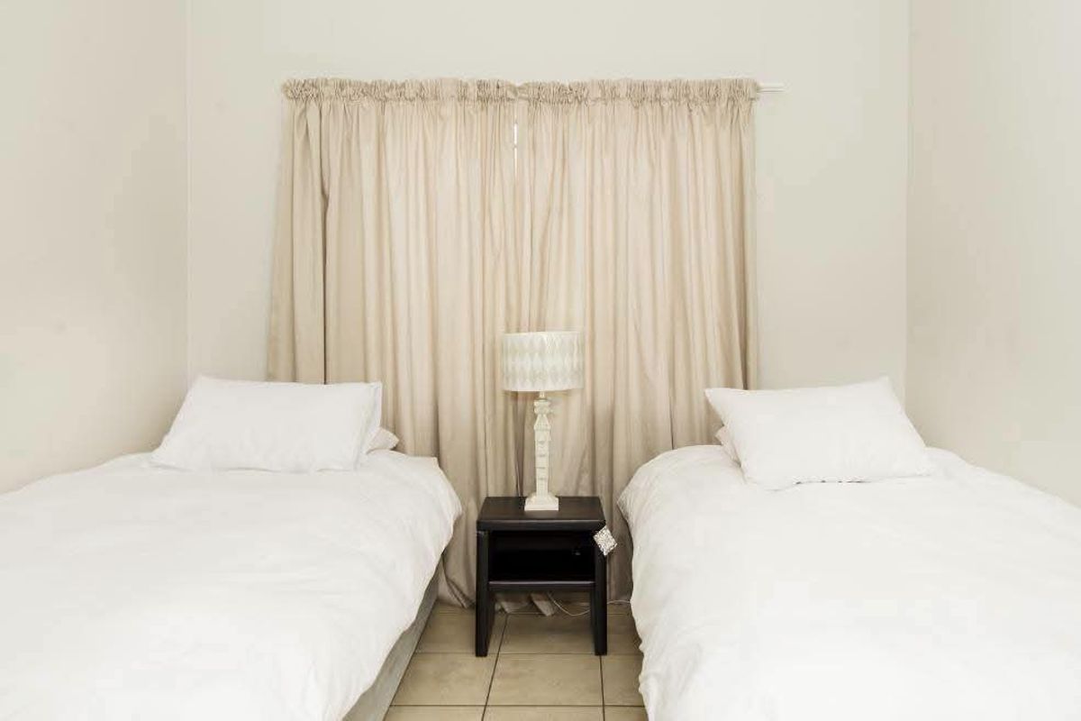A simple bedroom featuring neutral wall tones, tiled flooring, and a window dressed with floor-to-ceiling curtains.
