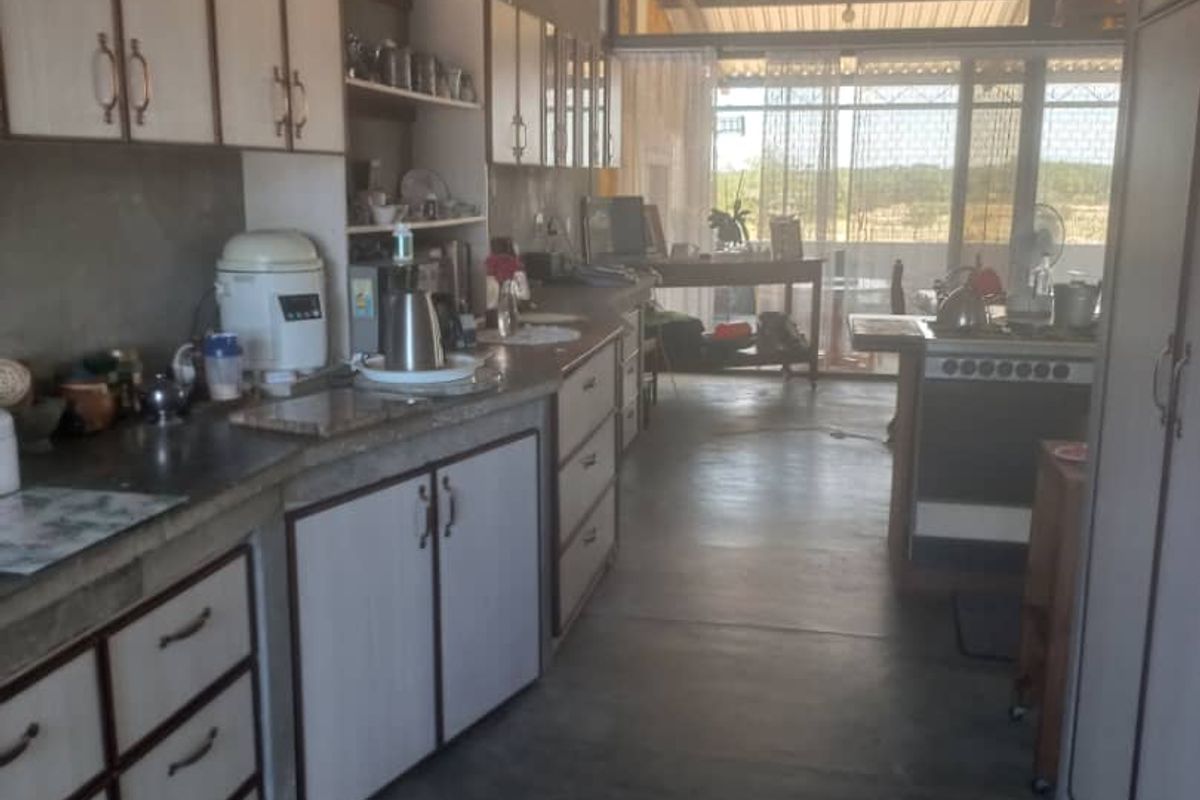 A rustic kitchen area featuring built-in cabinetry, concrete countertops, and an open-plan layout leading to an outdoor space.