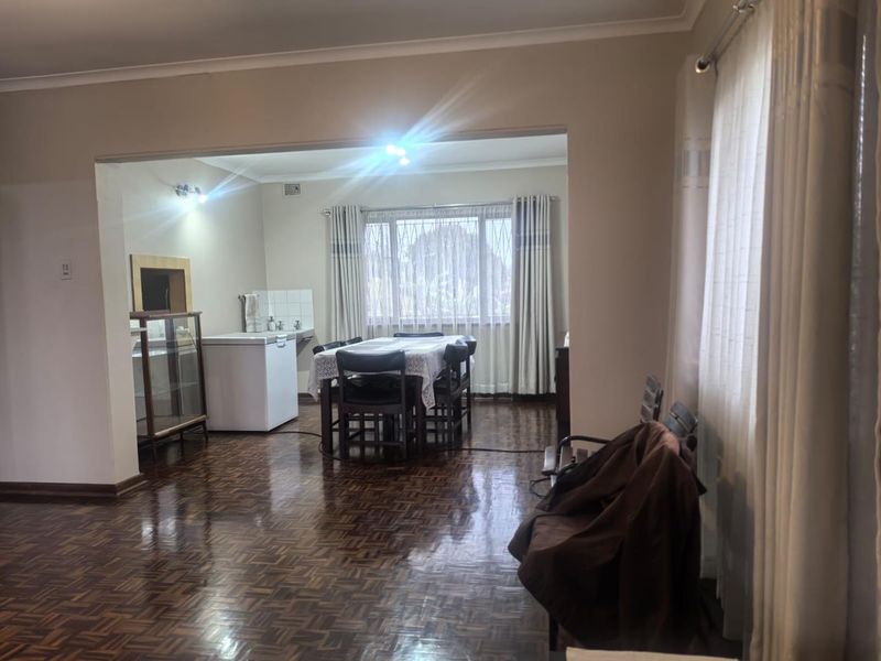 Open-plan living and dining area featuring polished parquet flooring, neutral wall tones, and large windows with security bars.