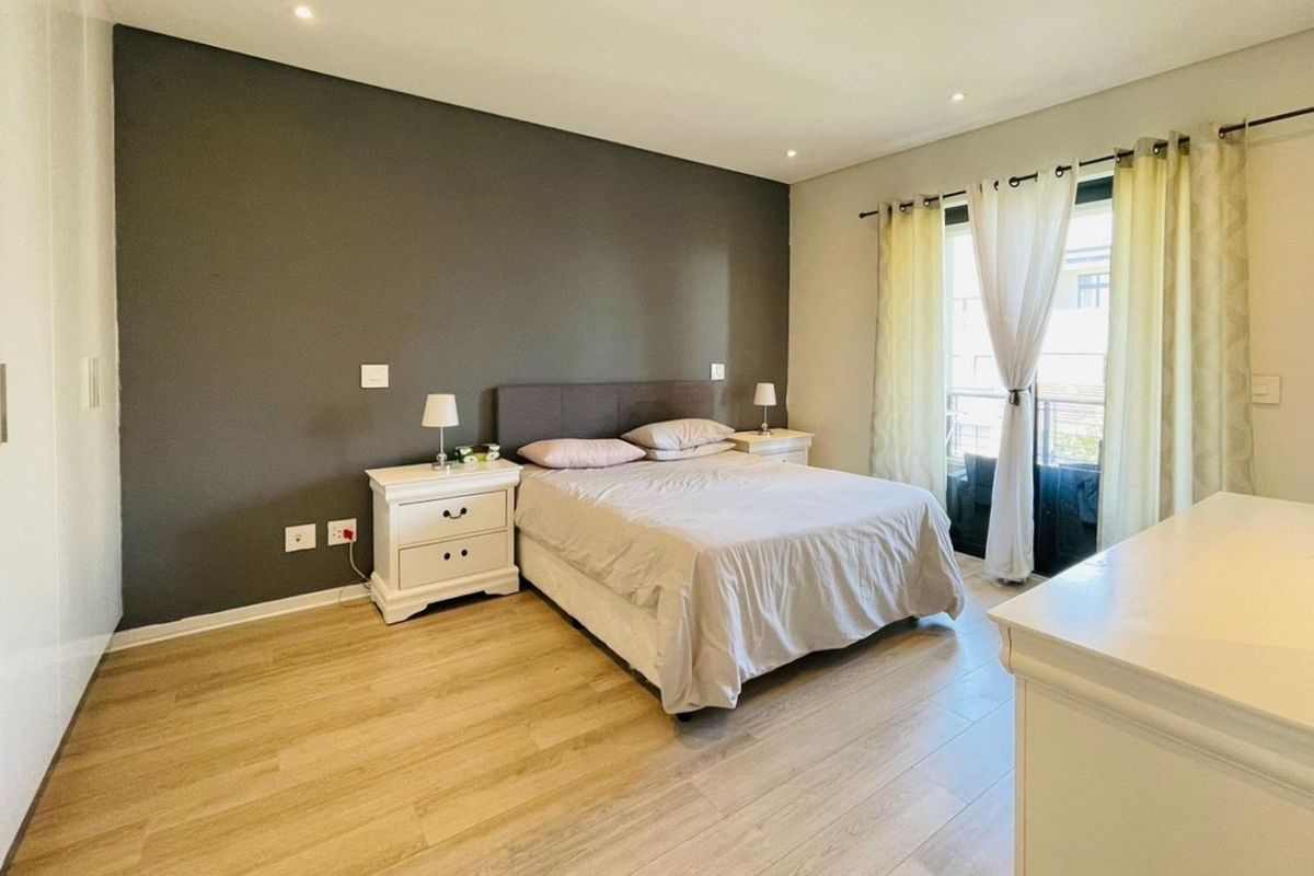 A well-maintained bedroom featuring light wood-look flooring, a dark accent wall, and sliding glass doors leading to a private balcony.
