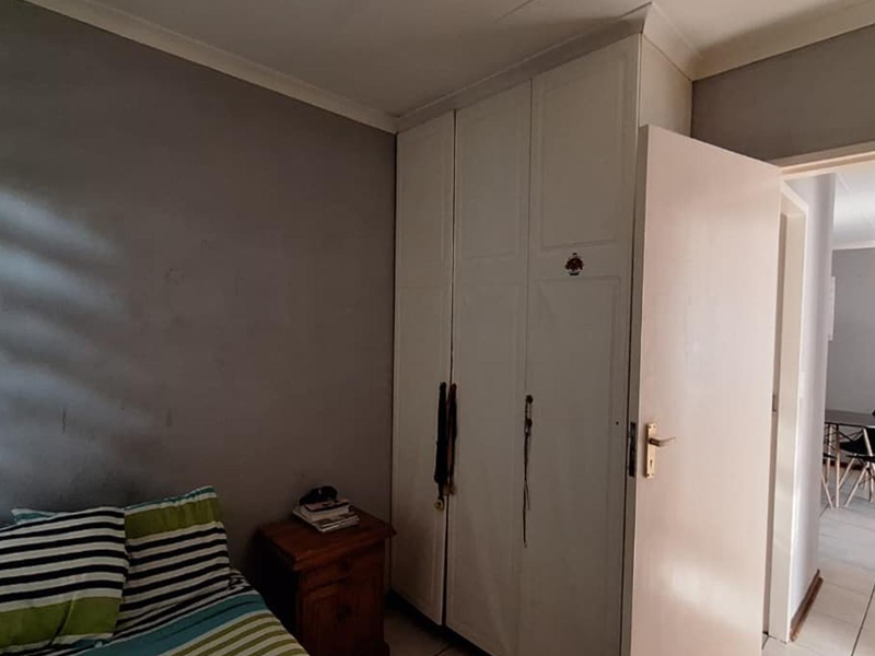 A bedroom featuring built-in cupboards, tiled flooring, and coved cornices, with a view into the adjacent living area.