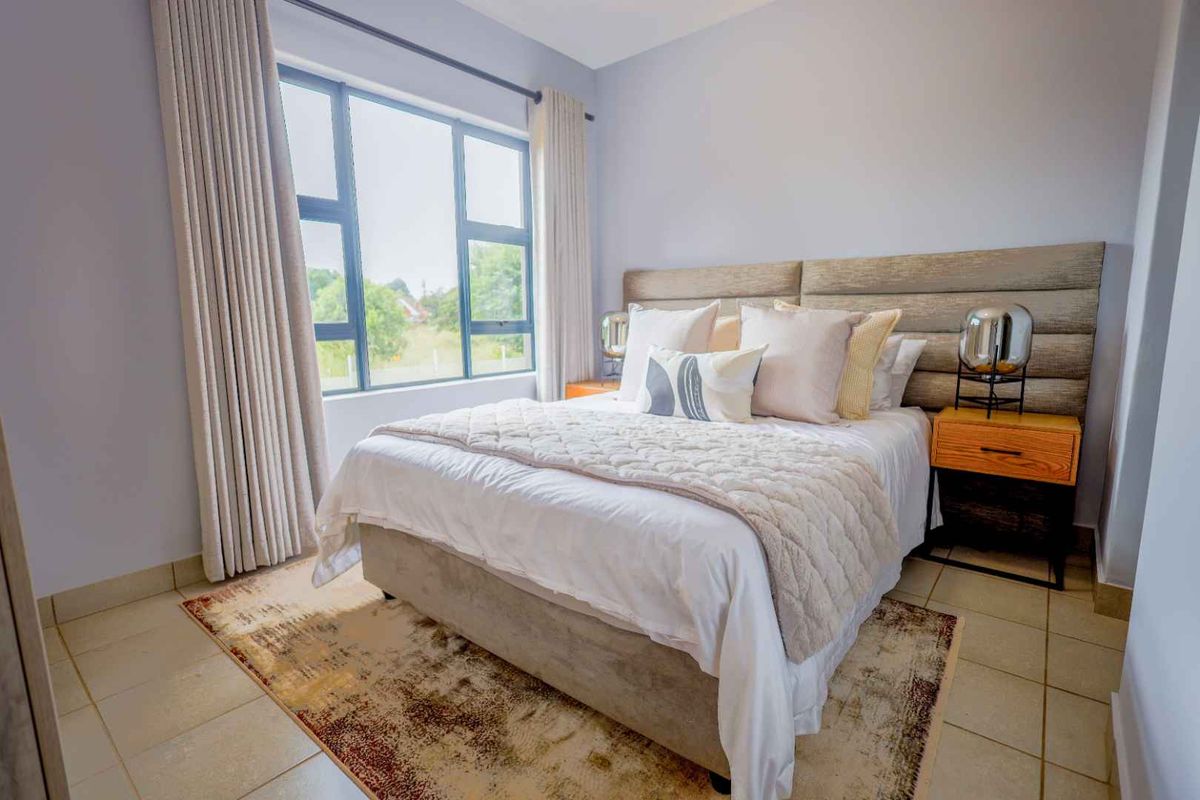 A well-lit bedroom featuring tiled flooring, a large window with curtain tracks, and neutral wall finishes.