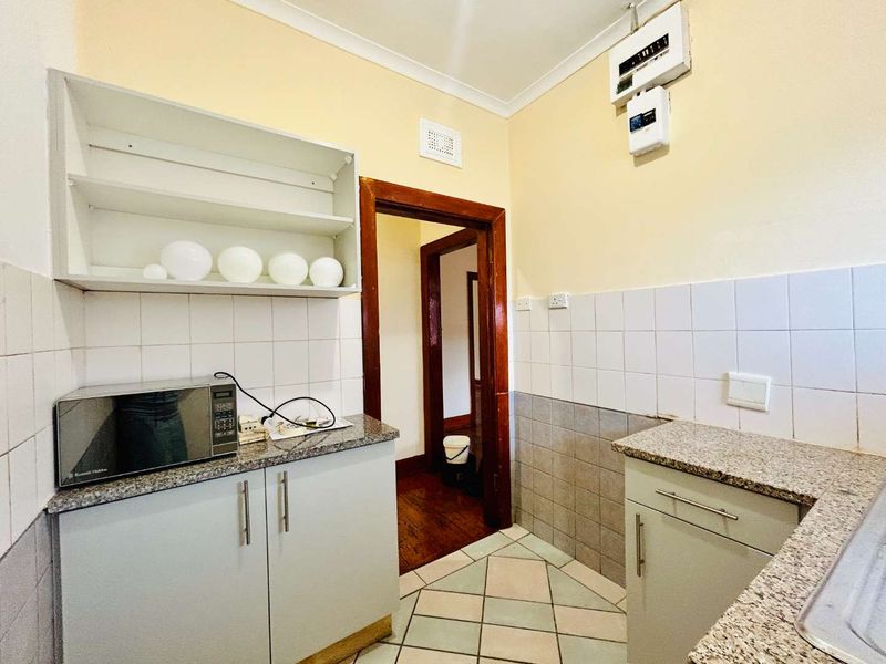 A functional kitchen featuring granite countertops, tiled splashbacks, and built-in cabinetry, providing a practical workspace with an adjacent hallway access.