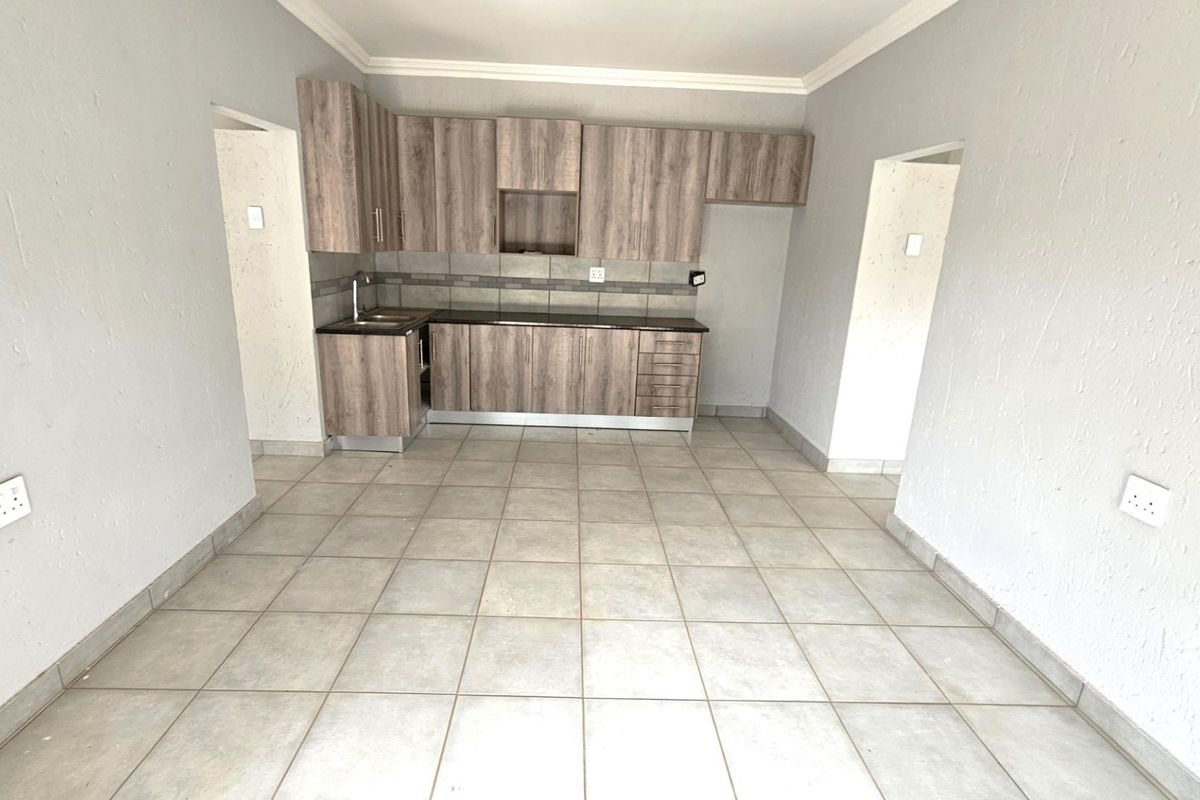 A functional kitchen area featuring wood-look cabinetry, dark countertops, and tiled flooring, presented in a clean, empty state ready for occupancy.