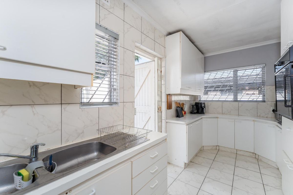 A functional kitchen featuring white cabinetry, marble-look wall tiles, tiled flooring, a stainless steel sink, and direct access to the exterior.