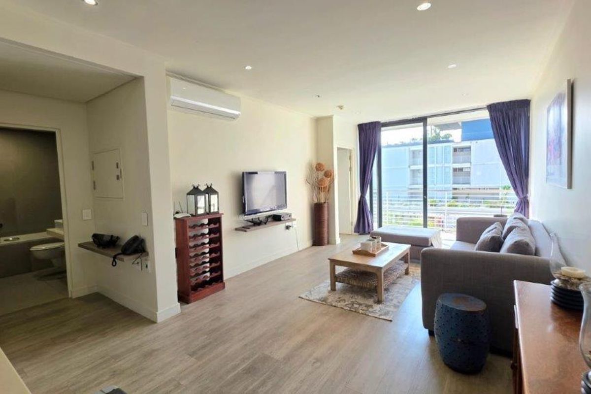 A bright, open-plan living area featuring laminate flooring, recessed lighting, and a split-system air conditioner, with direct access to a private balcony.