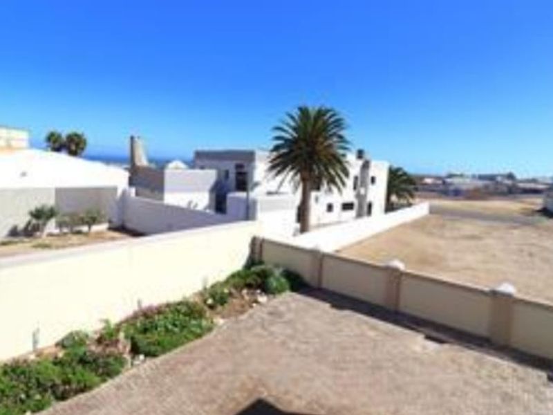 A rear exterior view featuring a paved courtyard, boundary wall, and landscaped garden beds with a view of the surrounding neighborhood.