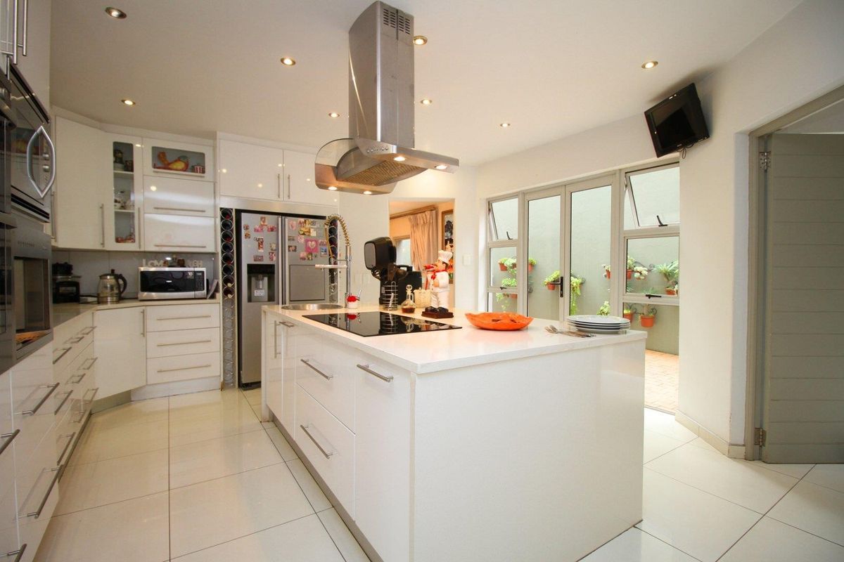 Modern kitchen featuring a central island with a built-in hob, stainless steel extractor fan, sleek white cabinetry, and tiled flooring with direct patio access.