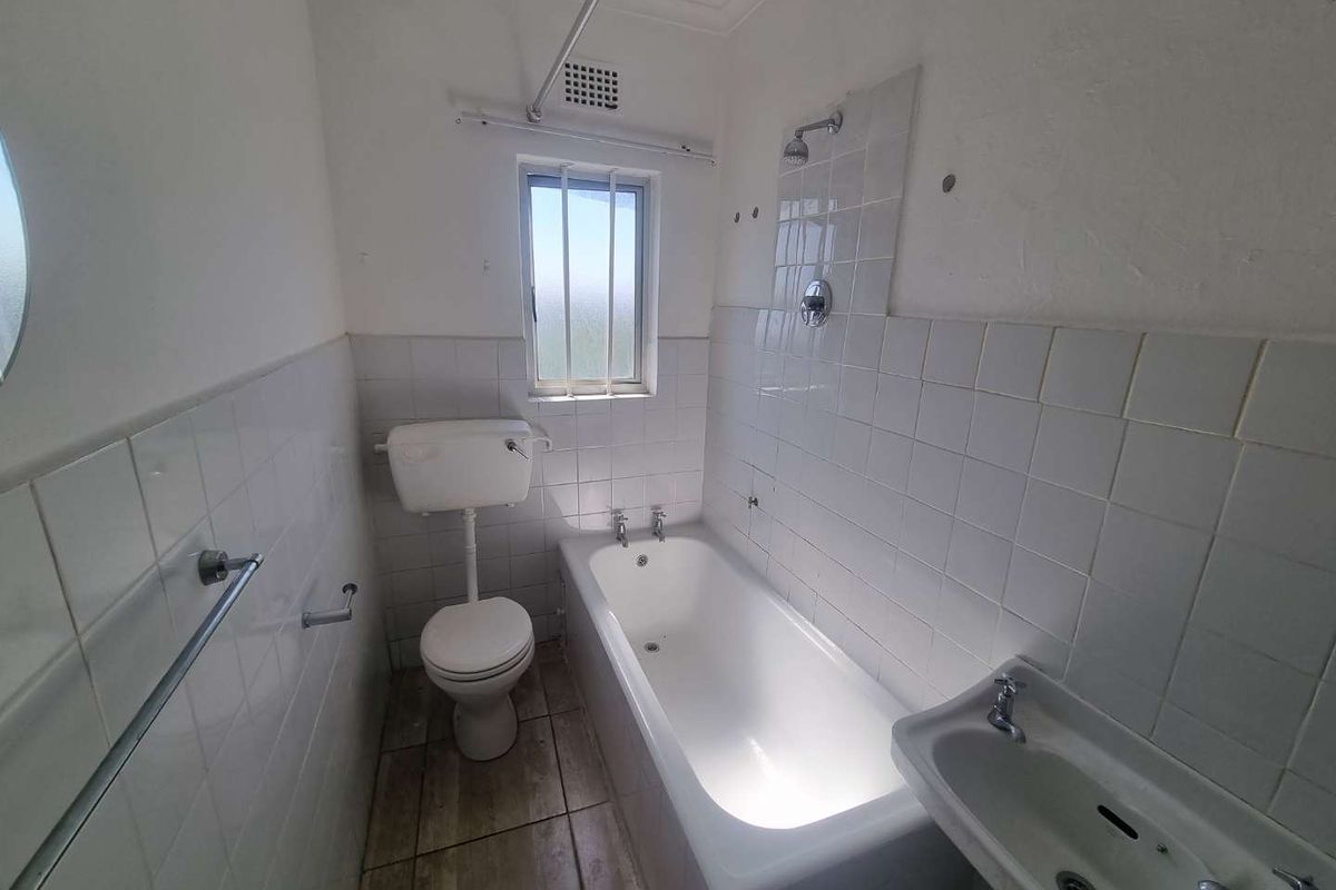 A dated bathroom featuring a bathtub, toilet, and wall-mounted basin with white wall tiling and floor tiles, requiring cosmetic updates.