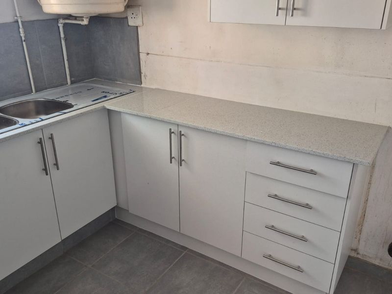 A kitchen area featuring white cabinetry, granite countertops, and a double bowl stainless steel sink, currently requiring wall finishing and electrical completion.