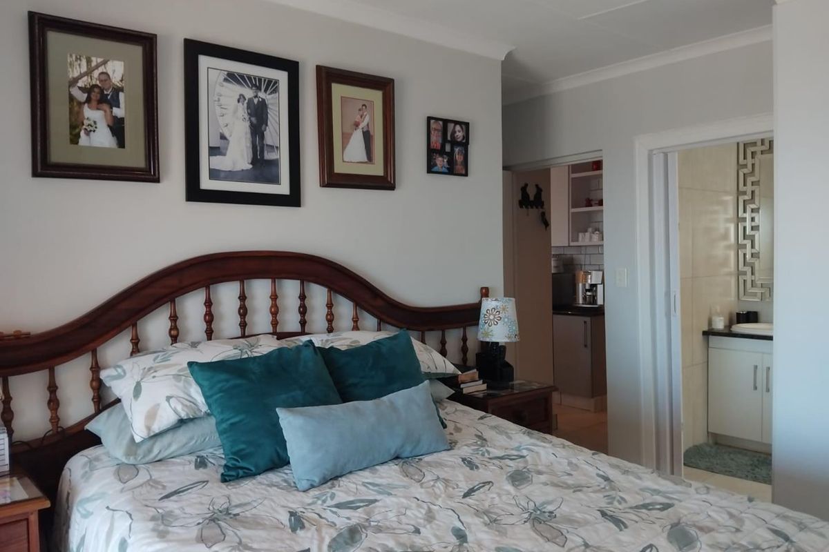 A bedroom featuring a wooden headboard, with an adjacent en-suite bathroom and a glimpse of a kitchen area in the background.