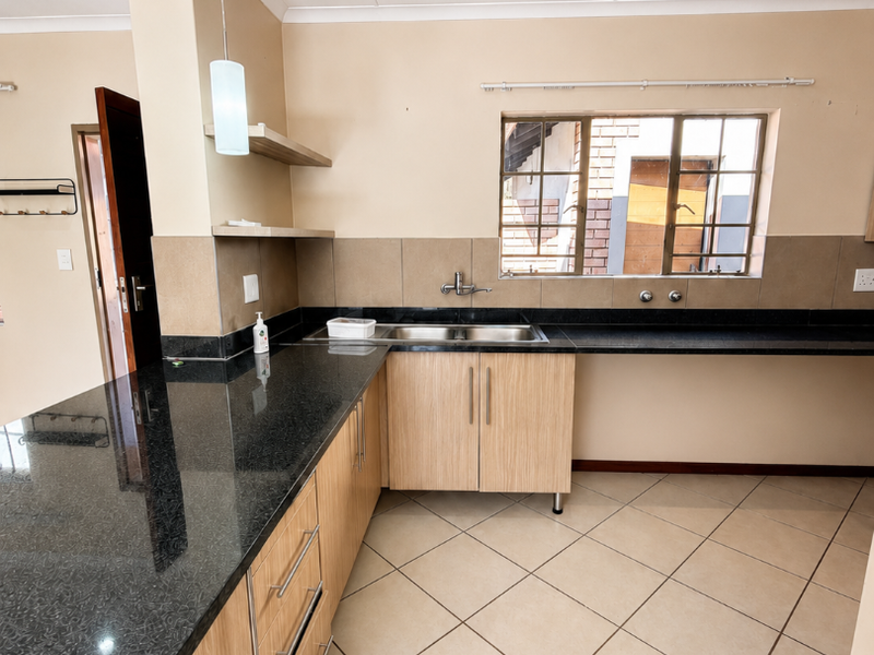 A functional kitchen featuring granite countertops, light wood cabinetry, double basin sink, and tiled flooring, offering a clean and practical workspace.