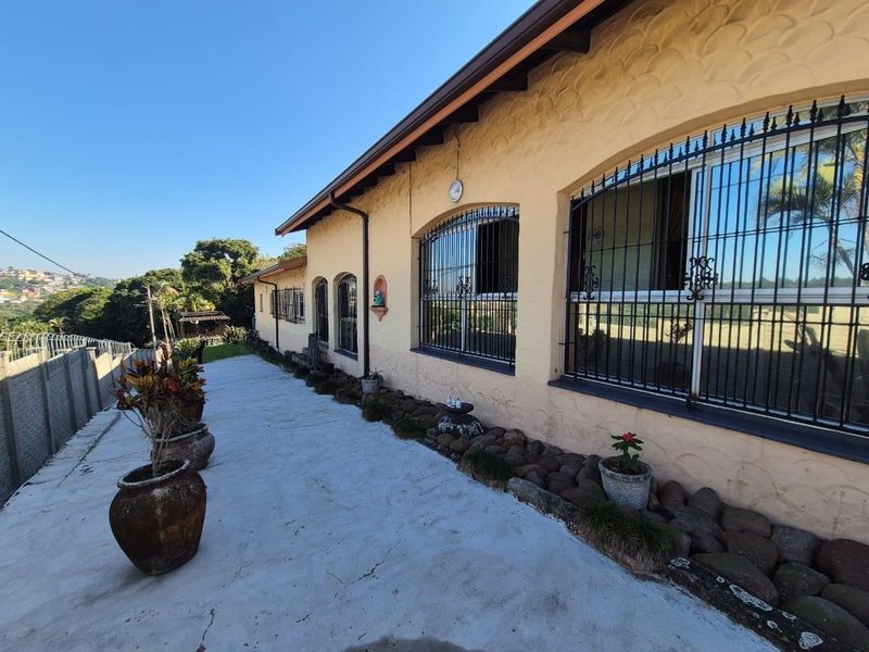 Rear exterior view of the property featuring a concrete patio, arched windows with security bars, and textured stucco walls.