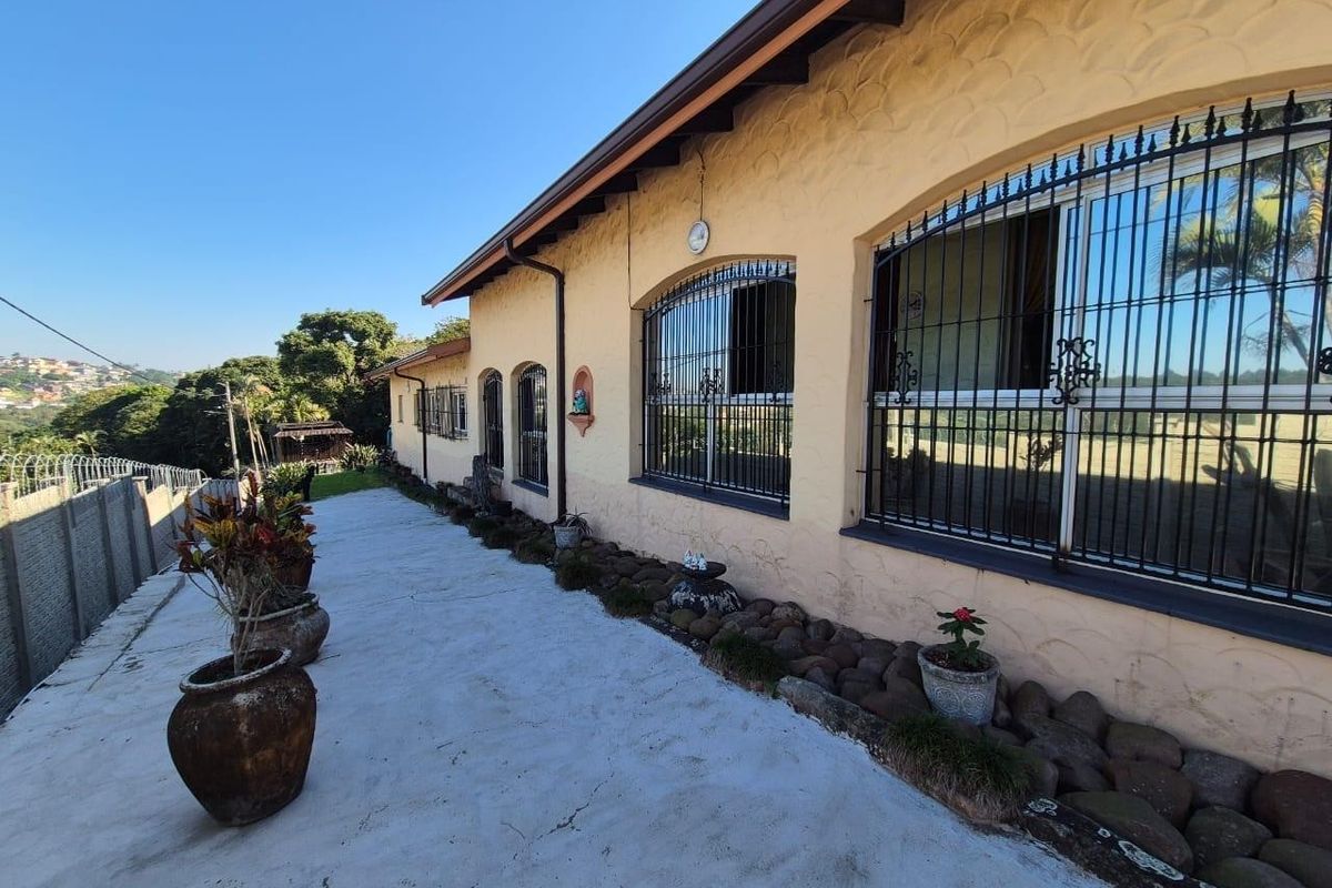 Rear exterior view of the property featuring a concrete patio, arched windows with security bars, and textured stucco walls.