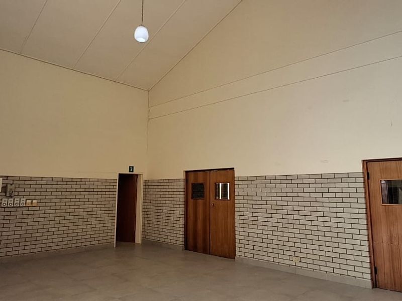 Spacious, empty living area featuring high vaulted ceilings, tiled flooring, and exposed brick accents, offering a versatile blank canvas for interior design.