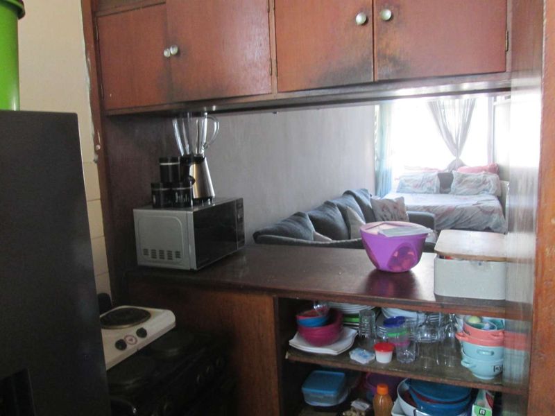 A compact kitchen area featuring built-in wooden cabinetry and a functional countertop, with a view through to the adjacent living and bedroom space.