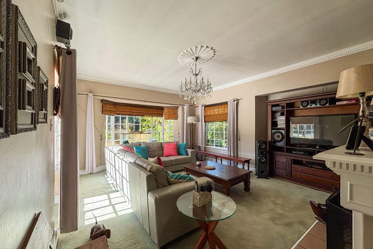 Spacious living room featuring a built-in wooden entertainment unit, decorative ceiling rose with chandelier, and large windows allowing for natural light.