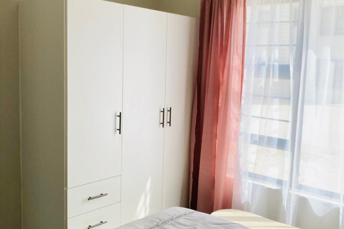 A bright bedroom featuring a clean, white built-in wardrobe and natural light filtering through the window.
