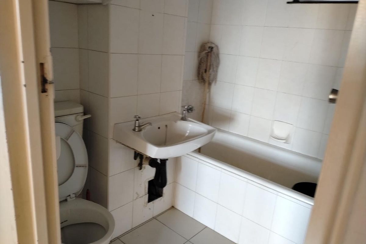 A dated bathroom featuring a standard bathtub, wall-mounted basin, and toilet with white tiled walls and flooring.