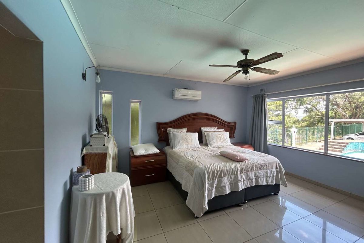 Spacious bedroom featuring large format floor tiles, a ceiling fan, and a wall-mounted air conditioning unit with views of the pool area.