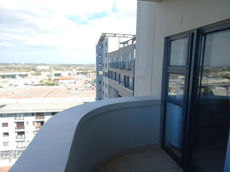 A private balcony featuring tiled flooring and a solid railing, offering an elevated view of the surrounding urban landscape.