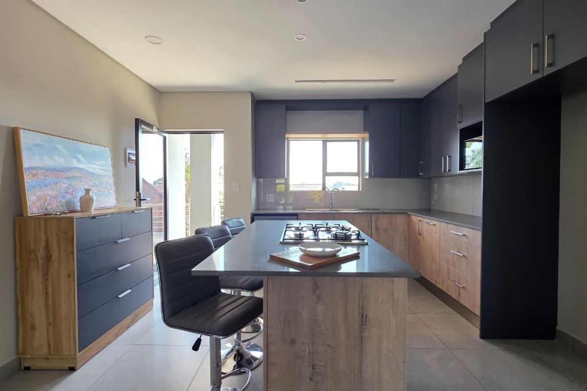 Modern kitchen featuring a central island with a gas cooktop, sleek two-tone cabinetry, stone countertops, and direct access to an outdoor balcony area.