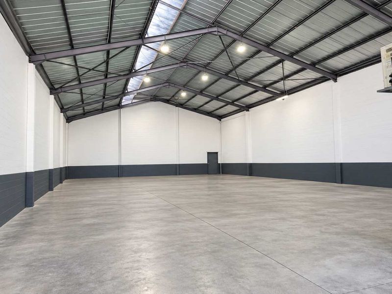 Spacious industrial warehouse unit featuring high ceilings with exposed steel trusses, polished concrete flooring, and a wall-mounted air conditioning unit.
