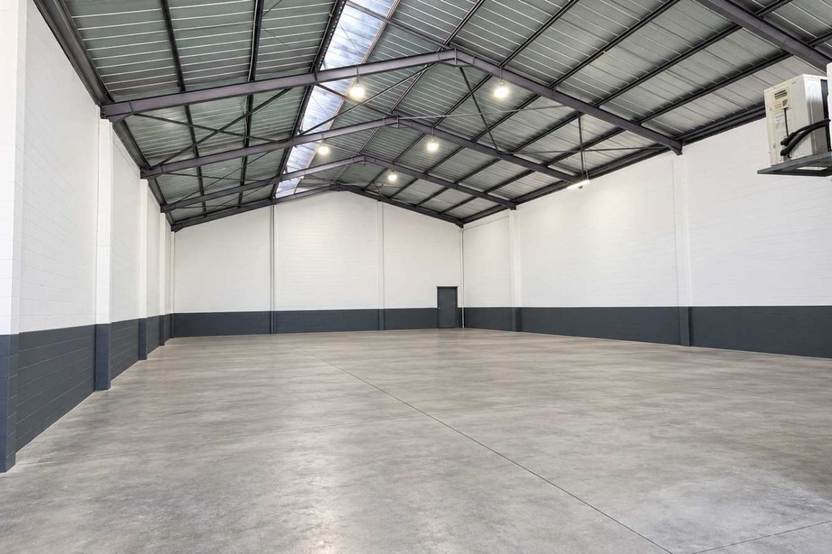 Spacious industrial warehouse unit featuring high ceilings with exposed steel trusses, polished concrete flooring, and a wall-mounted air conditioning unit.