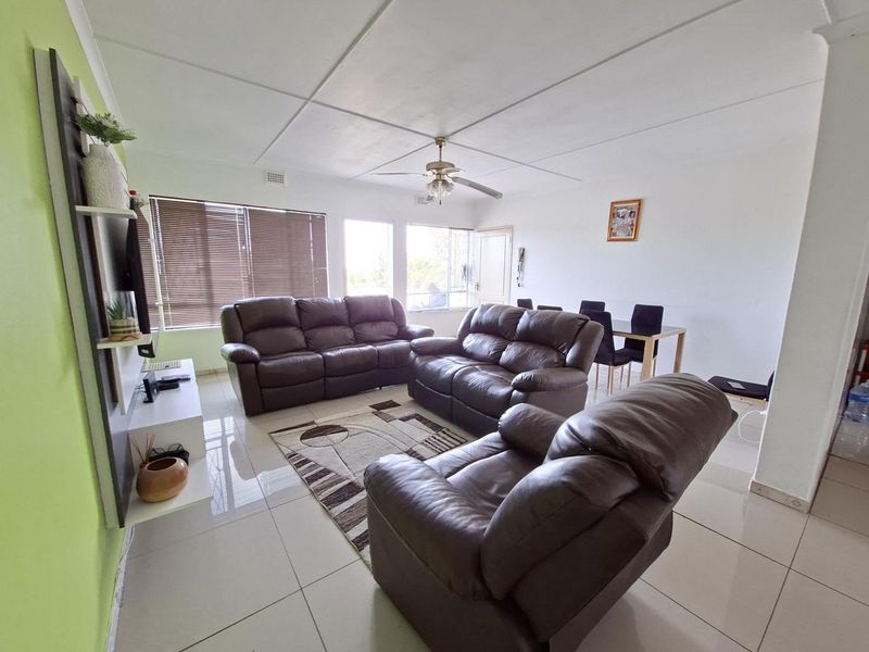 Open-plan living and dining area featuring tiled flooring, a ceiling fan, and large windows with venetian blinds.
