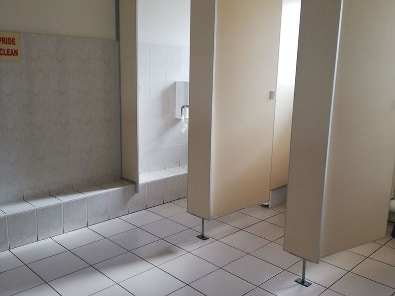 A functional office bathroom featuring tiled flooring, wall cladding, and multiple toilet cubicle partitions with a suspended ceiling.