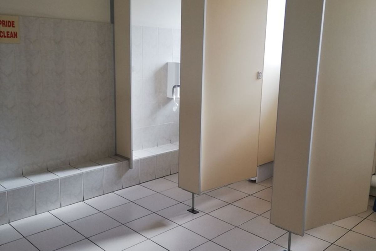 A functional office bathroom featuring tiled flooring, wall cladding, and multiple toilet cubicle partitions with a suspended ceiling.