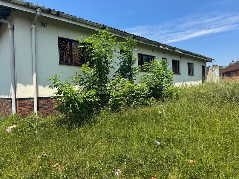 Rear exterior view of the property featuring a brick base, security bars on windows, and significant overgrown vegetation requiring maintenance.