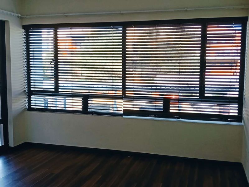 An empty living room featuring dark laminate flooring, large windows with venetian blinds, and a sliding glass door leading to an outdoor area.