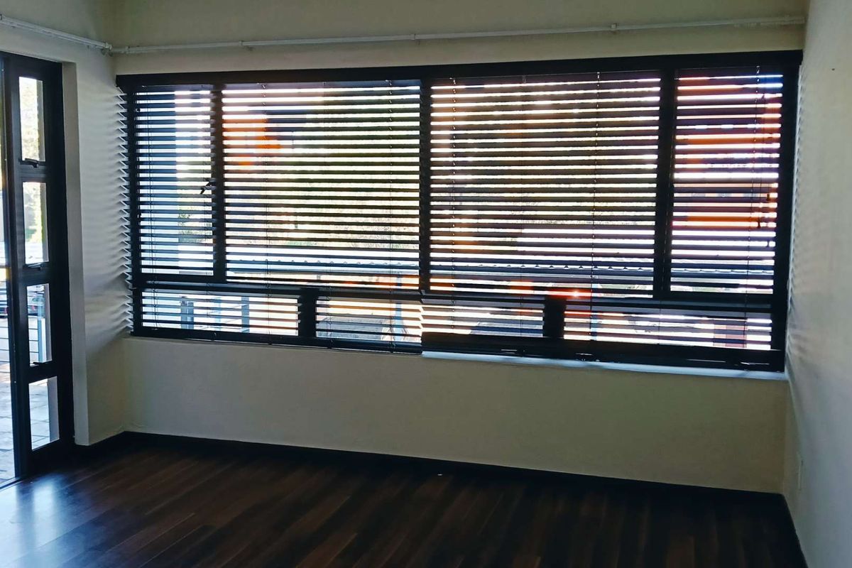 An empty living room featuring dark laminate flooring, large windows with venetian blinds, and a sliding glass door leading to an outdoor area.