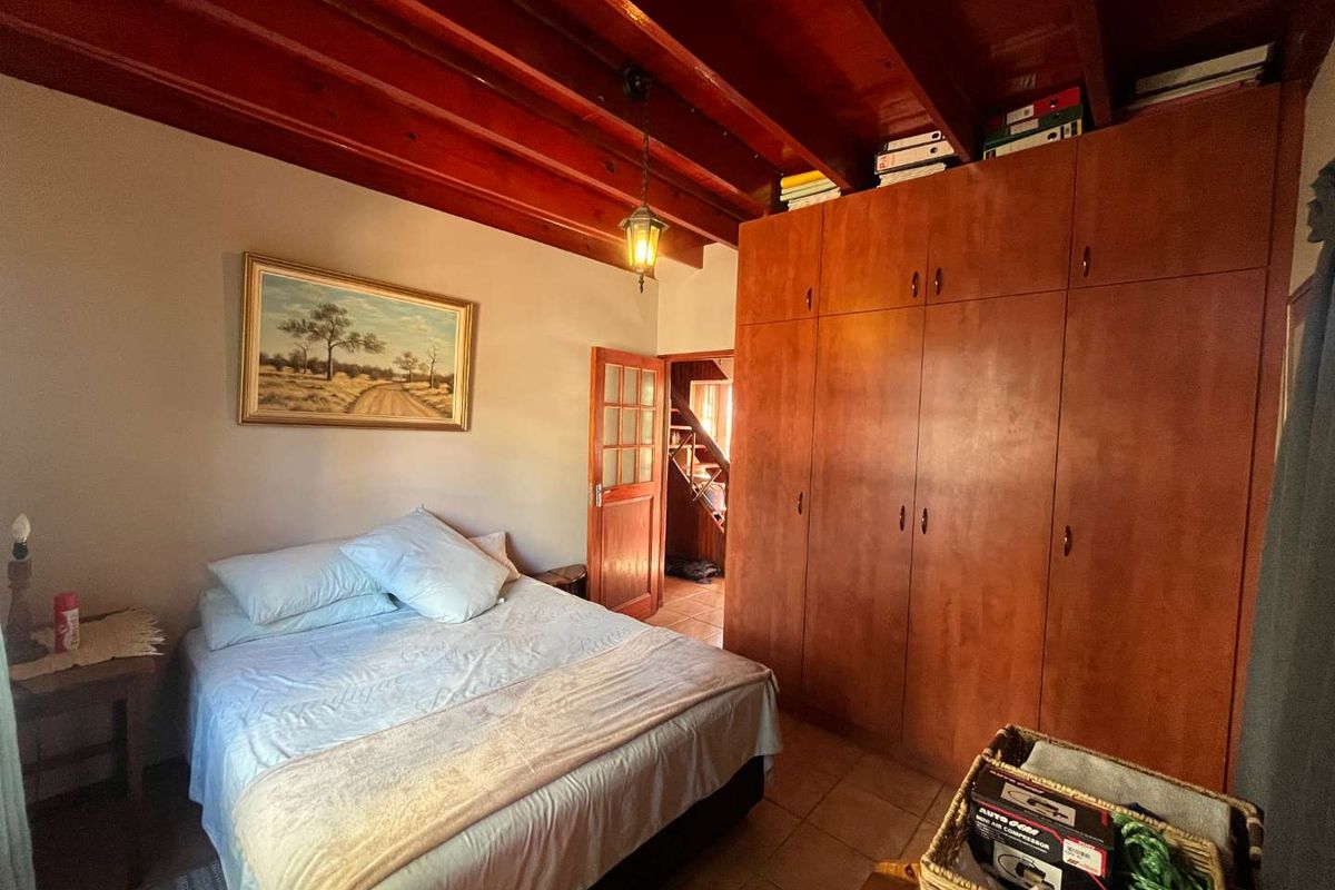 A cozy bedroom featuring exposed timber ceiling beams, tiled flooring, and extensive built-in wooden cabinetry for storage.