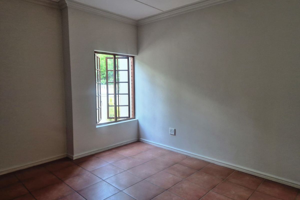 A bright, empty bedroom featuring neutral walls, tiled flooring, and a classic casement window with crown molding detail.