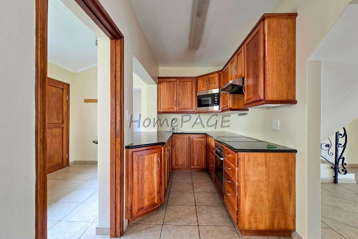 A functional kitchen featuring wooden cabinetry, stone countertops, and built-in appliances, including an oven, microwave, and extractor fan.
