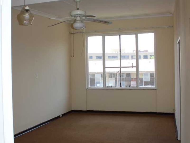 An empty living room featuring carpet flooring, a ceiling fan, and a large window providing natural light.