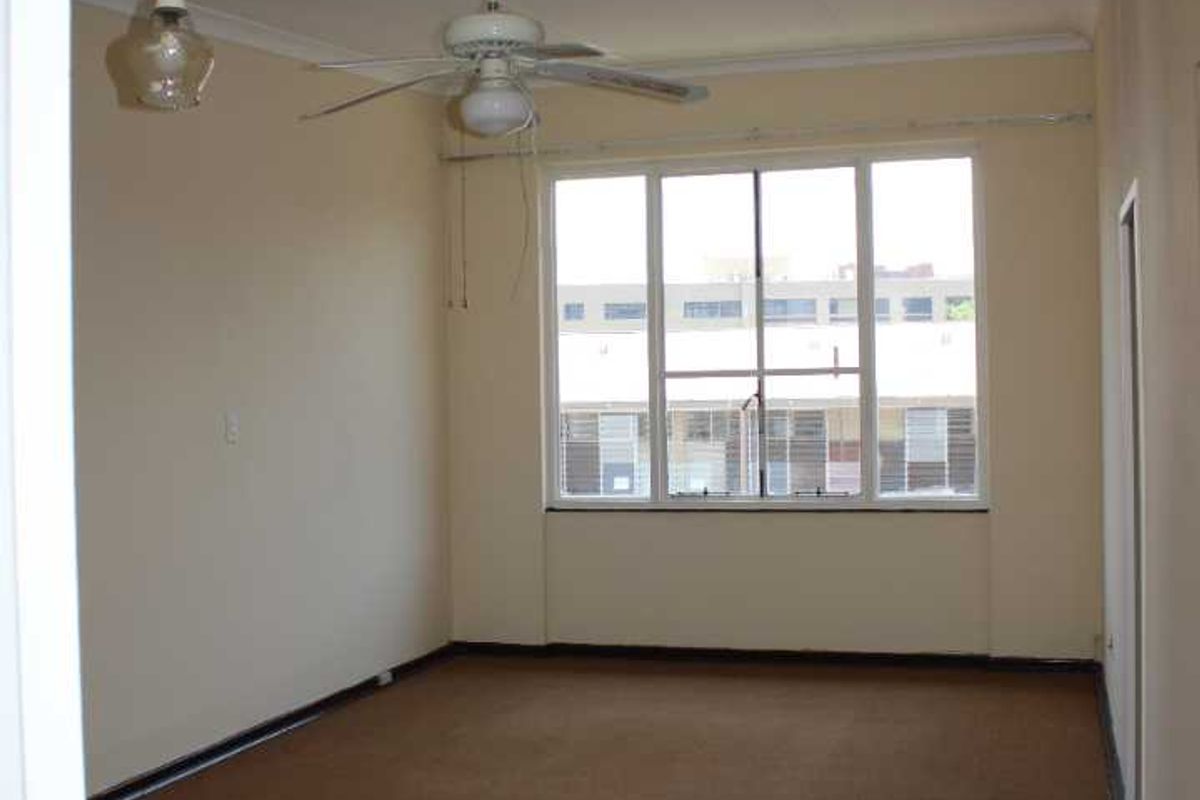 An empty living room featuring carpet flooring, a ceiling fan, and a large window providing natural light.