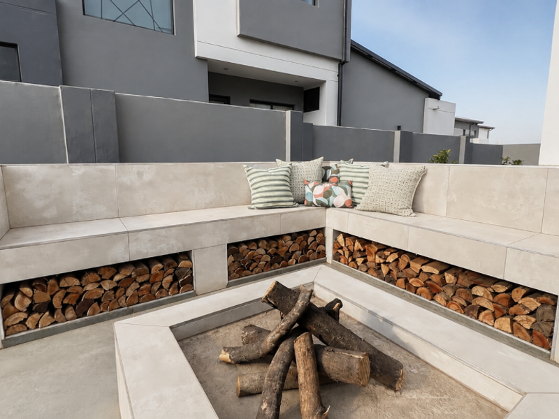 Modern outdoor patio area featuring a custom built-in tiled seating bench with integrated firewood storage and a central fire pit.