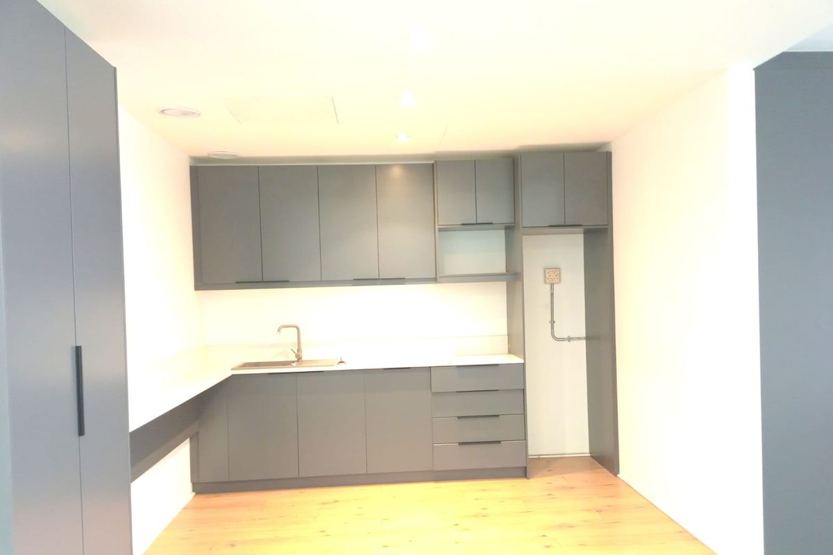 A modern, minimalist kitchenette featuring sleek grey cabinetry, a stainless steel sink, and light wood-look flooring in a clean, bright office space.