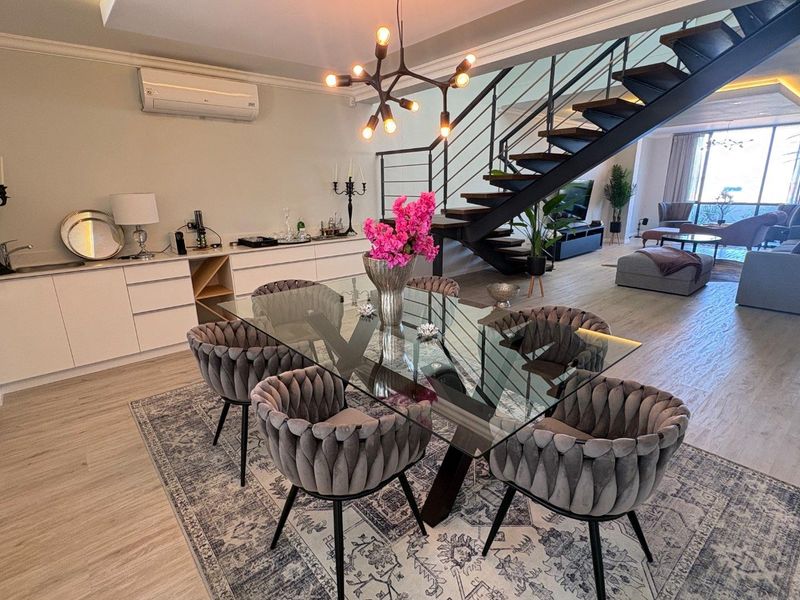 Modern open-plan living and dining area featuring a striking floating staircase, sleek built-in cabinetry, and high-quality finishes throughout.