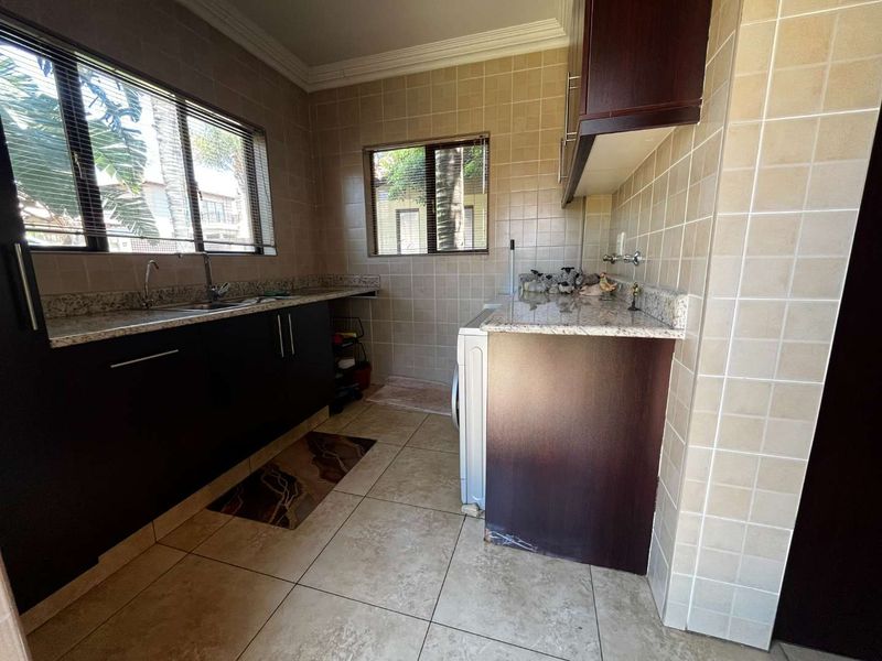 Functional laundry room featuring granite countertops, dark wood cabinetry, tiled splashbacks, and dedicated plumbing connections for appliances.