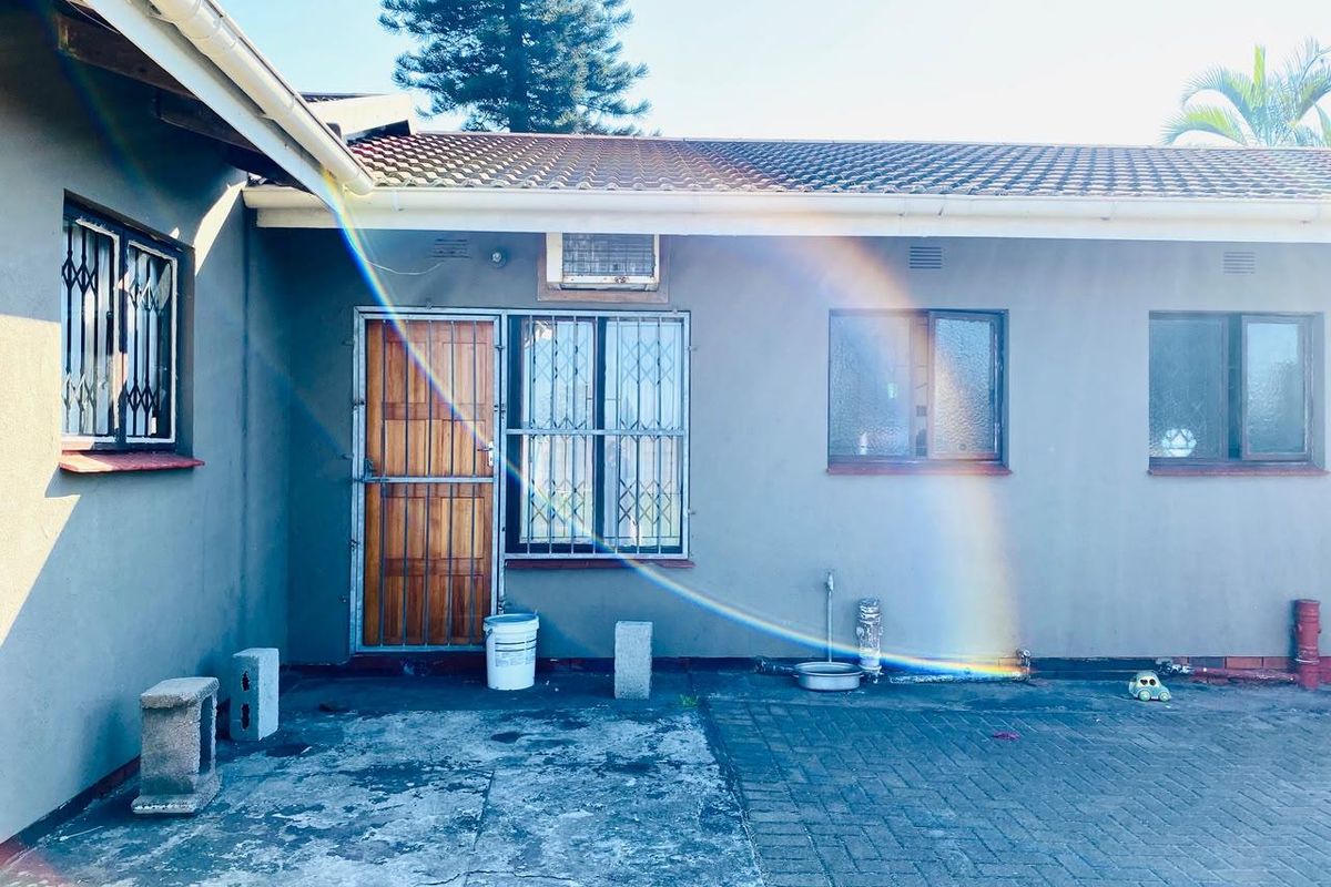Rear exterior view of the house featuring a paved courtyard, security gates on windows and doors, and a wall-mounted air conditioning unit.